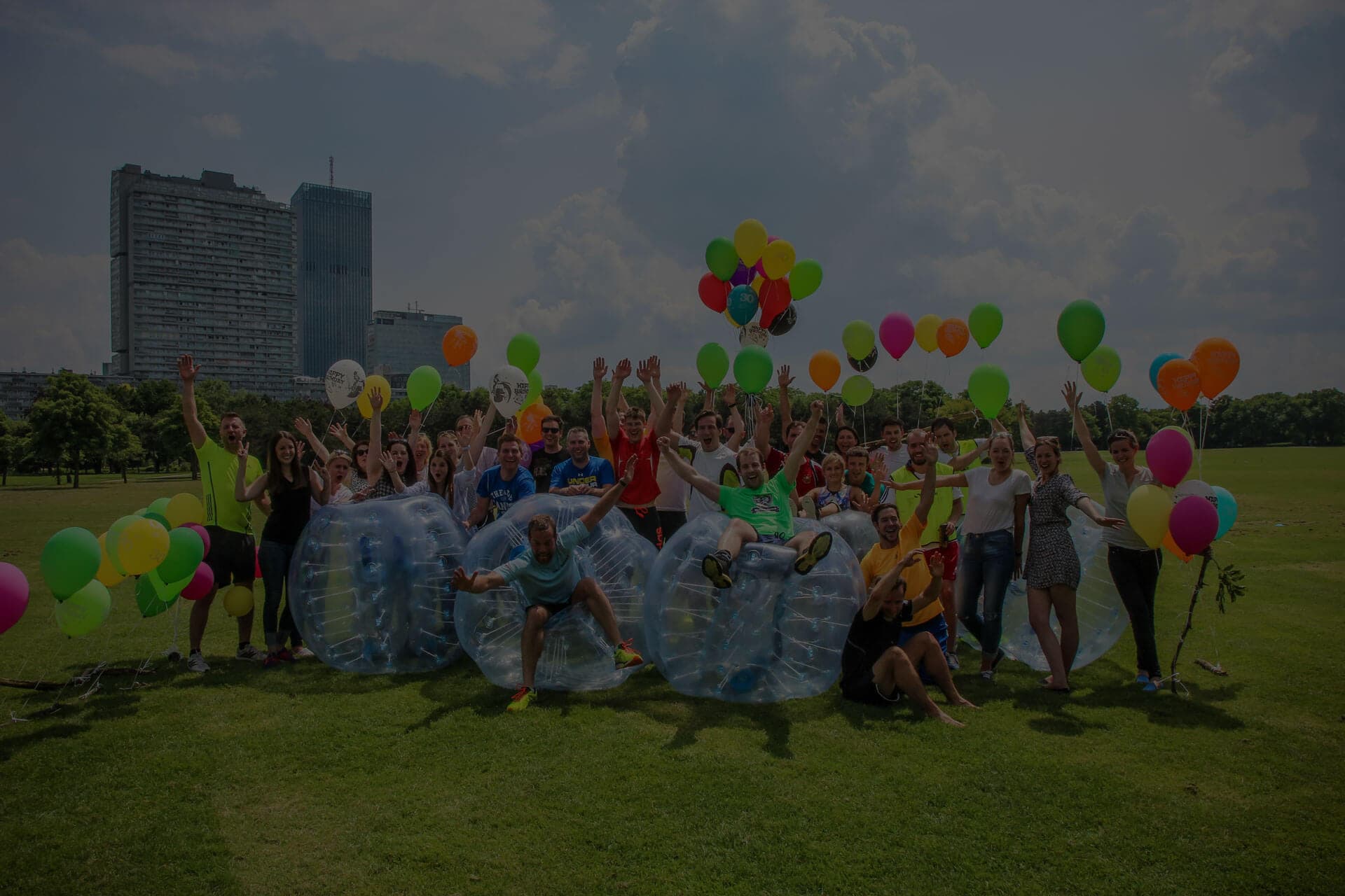 Group cheering on a park lawn behind transparent bubble soccer balls